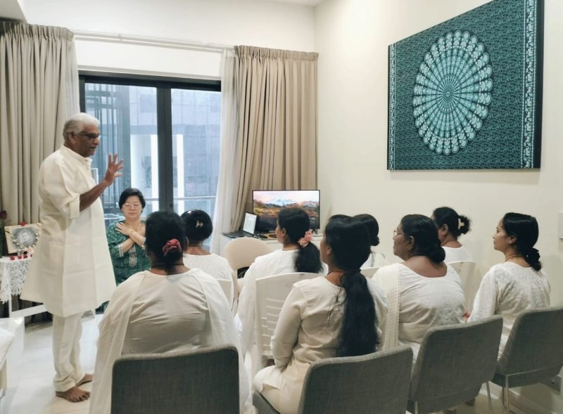 A Reiki master in traditional white attire conducting a Tera Mai™ Reiki training session in Kuala Lumpur, Malaysia, with a group of women dressed in white seated attentively in a serene indoor setting